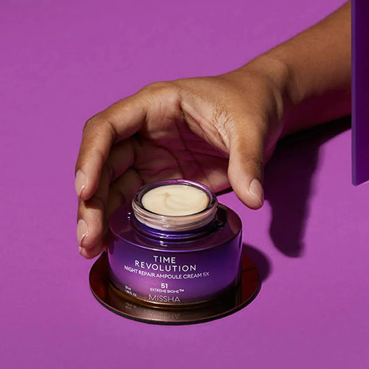 Missha Time Revolution Night Repair Ampoule Cream 5x 50ml – Hand präsentiert den Tiegel vor violettem Hintergrund