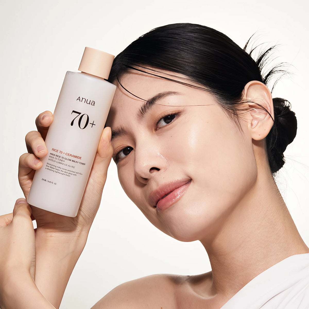 Anua Rice 70 Glow Milky Toner 250ml – Frau mit hochgestecktem Haar hält Flasche vors Gesicht
