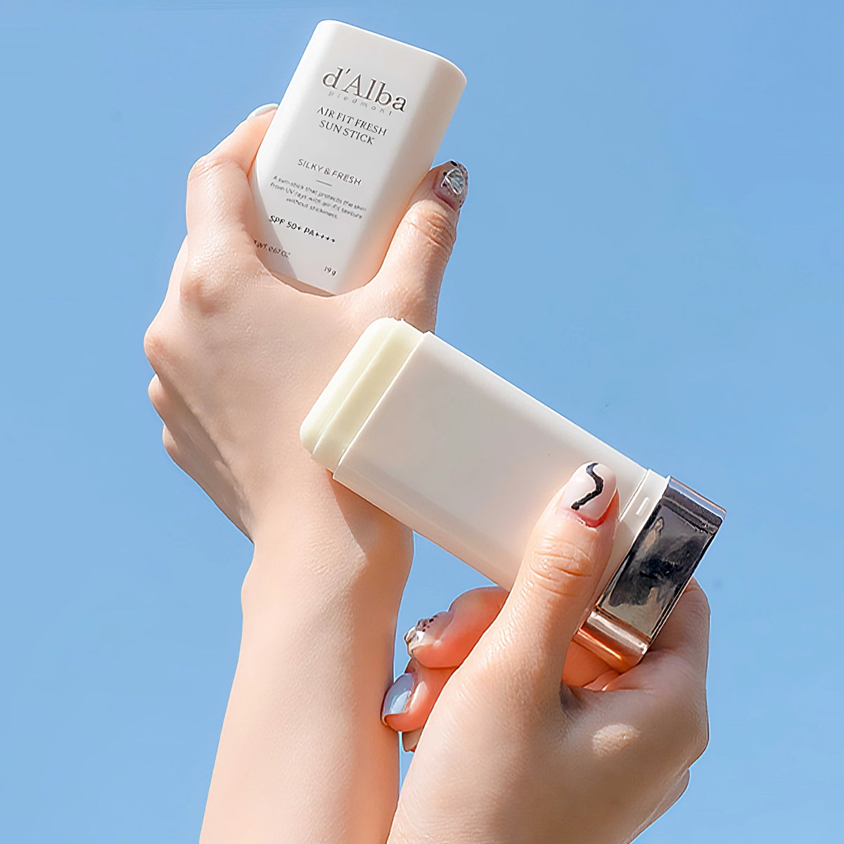 d'Alba Air Fit Fresh Sun Stick SPF50+/PA++++ 19g – zwei Hände halten einen weißen Karton vor blauem Himmel