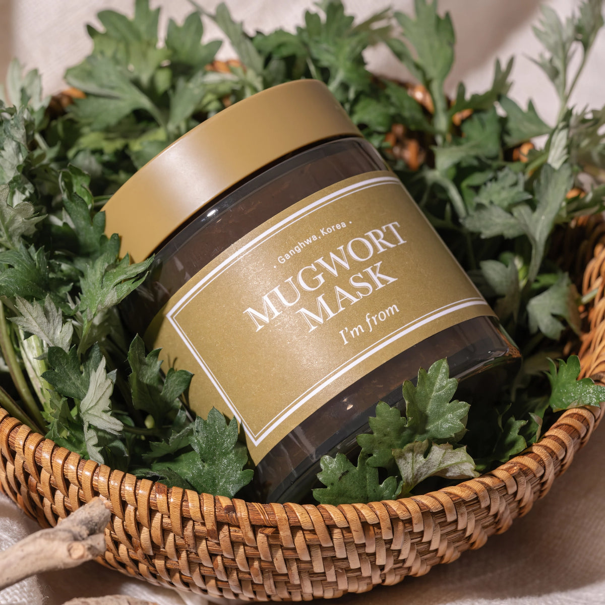 I'm From Mugwort Mask 110g – goldbrauner Tiegel mit braun-goldenem Etikett in einem Weidenkorb voller frischer Kräuter